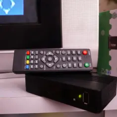 Pilot do telewizora i dekoder na białej półce.
